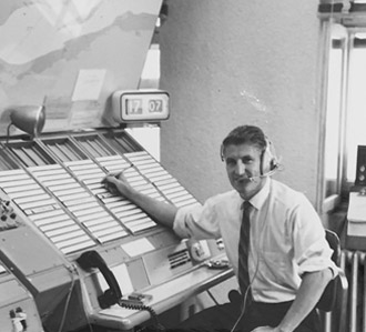 Lucien Misson travaillant comme opérateur radio, dans un centre d'opérations. Il sourit à la caméra.